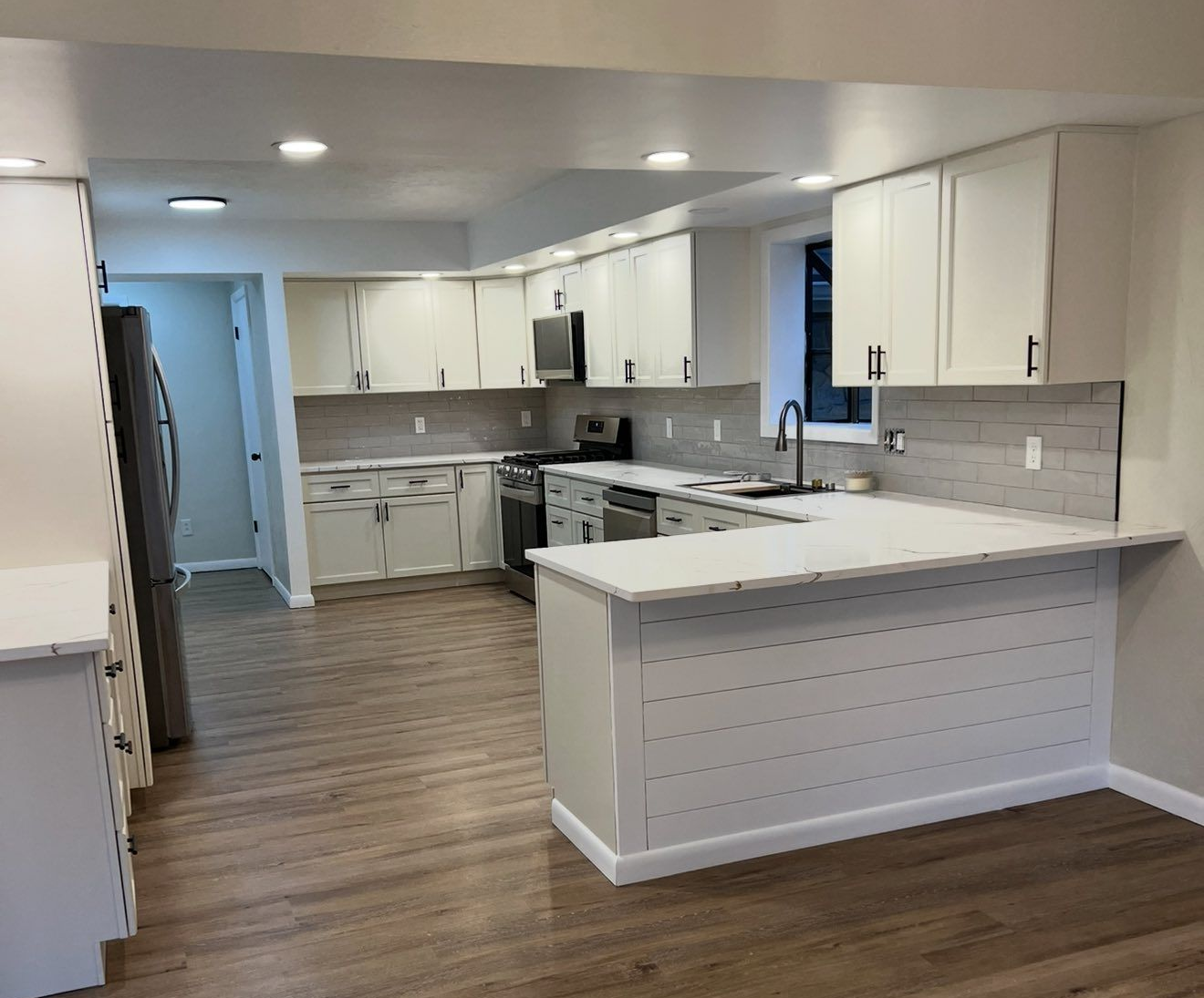Bright white kitchen with island, gray backsplash, and wood-look flooring in an empty home