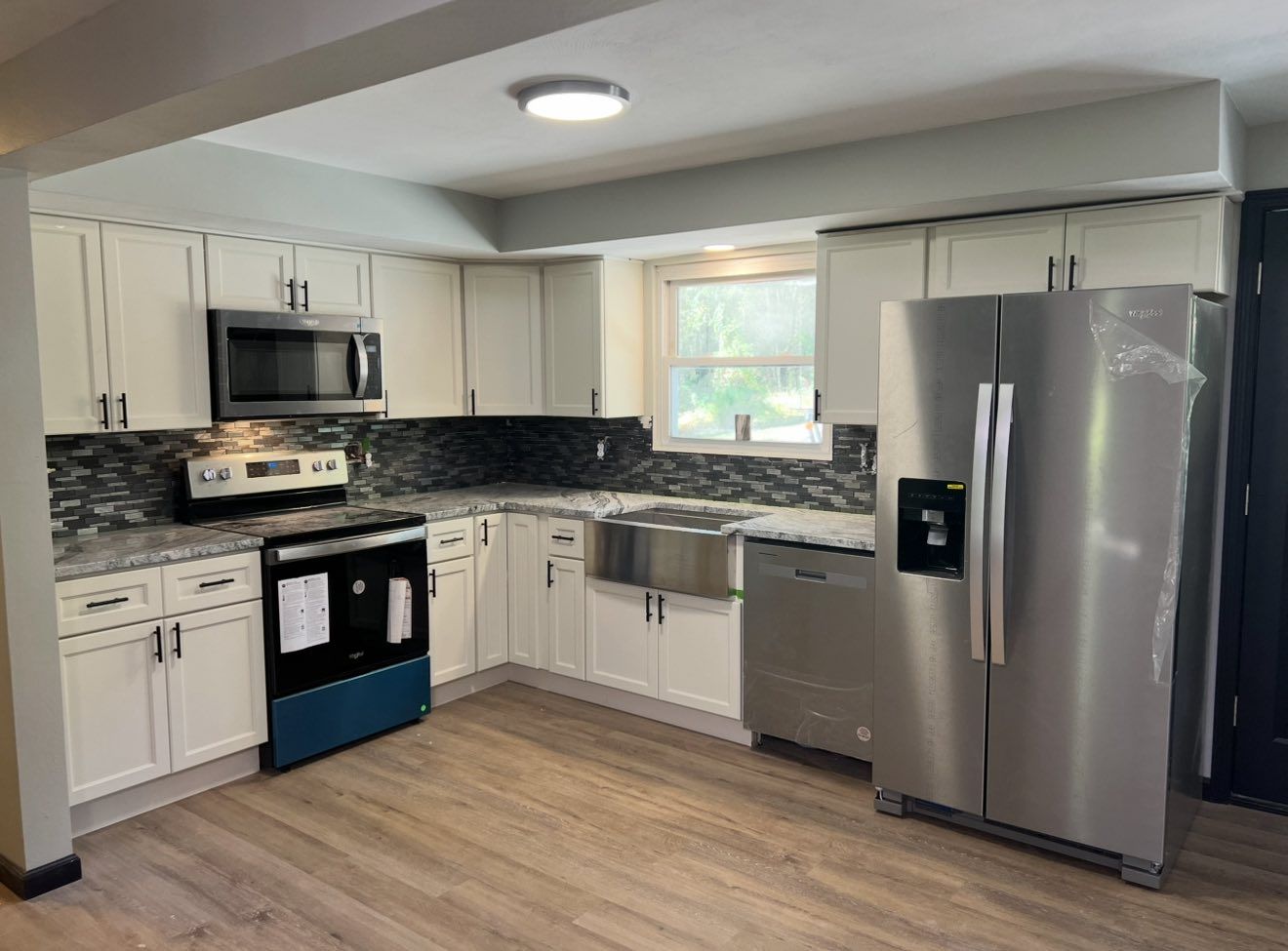 Modern kitchen with white cabinets, black backsplash, stainless appliances, and light wood flooring.