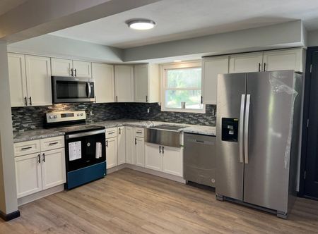 Modern kitchen with white cabinets, black backsplash, stainless appliances, and light wood flooring.