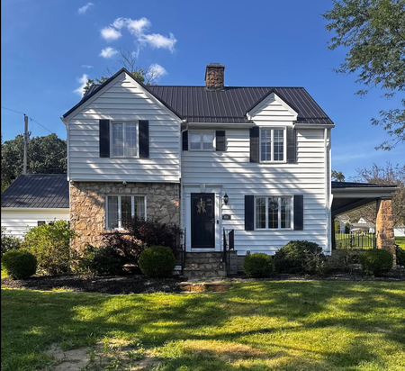 Two-story white house with black shutters and stone accents on a sunny lawn