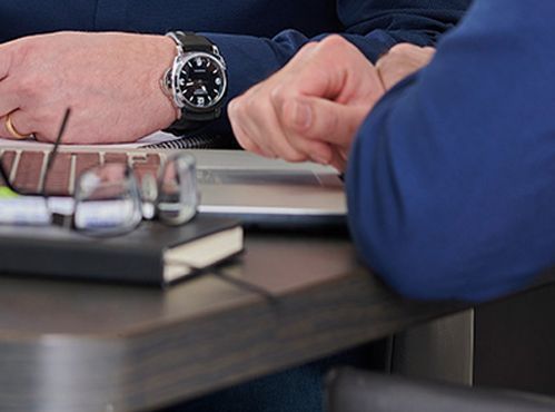 Een man met een horloge zit aan een tafel en gebruikt een laptop.