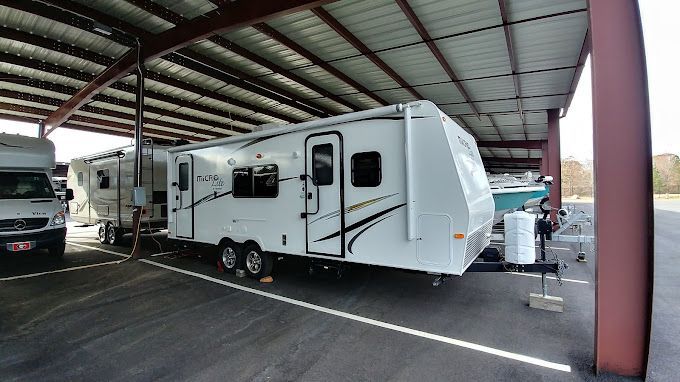 White travel trailer parked under a metal shelter with other vehicles.