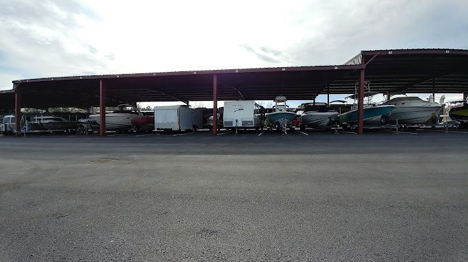 Boats stored under a large, covered structure, against a cloudy sky.