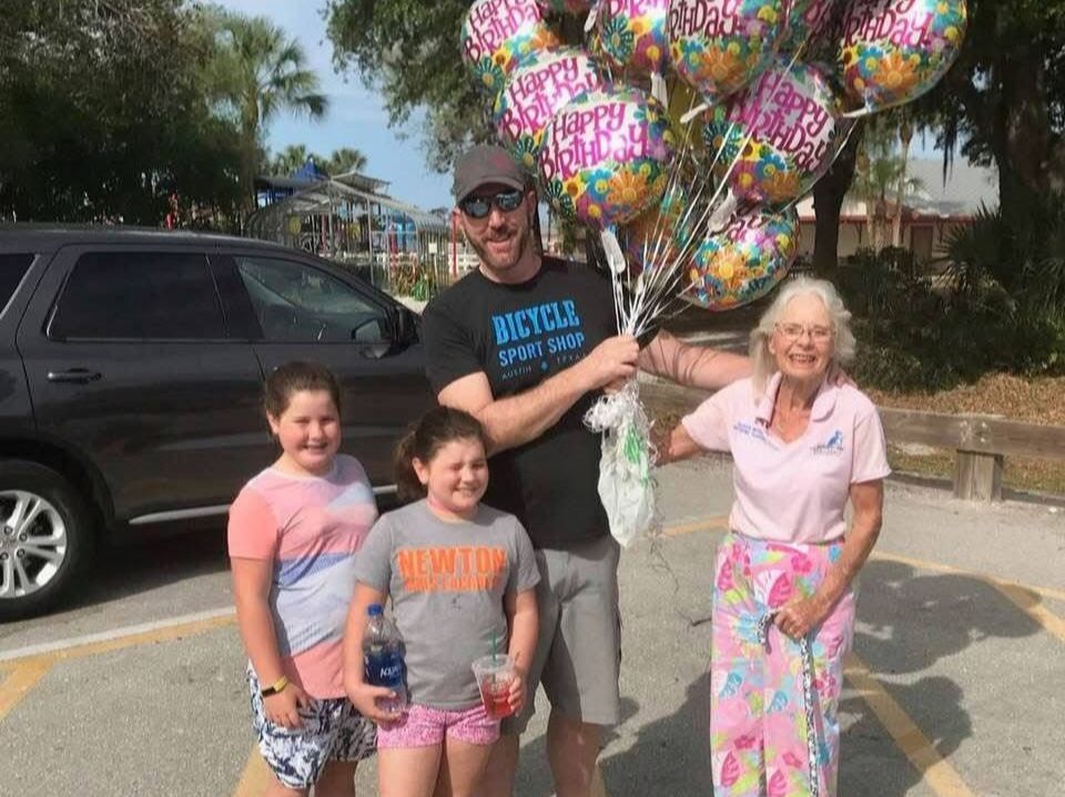 A man is holding a bunch of balloons in front of a group of people.