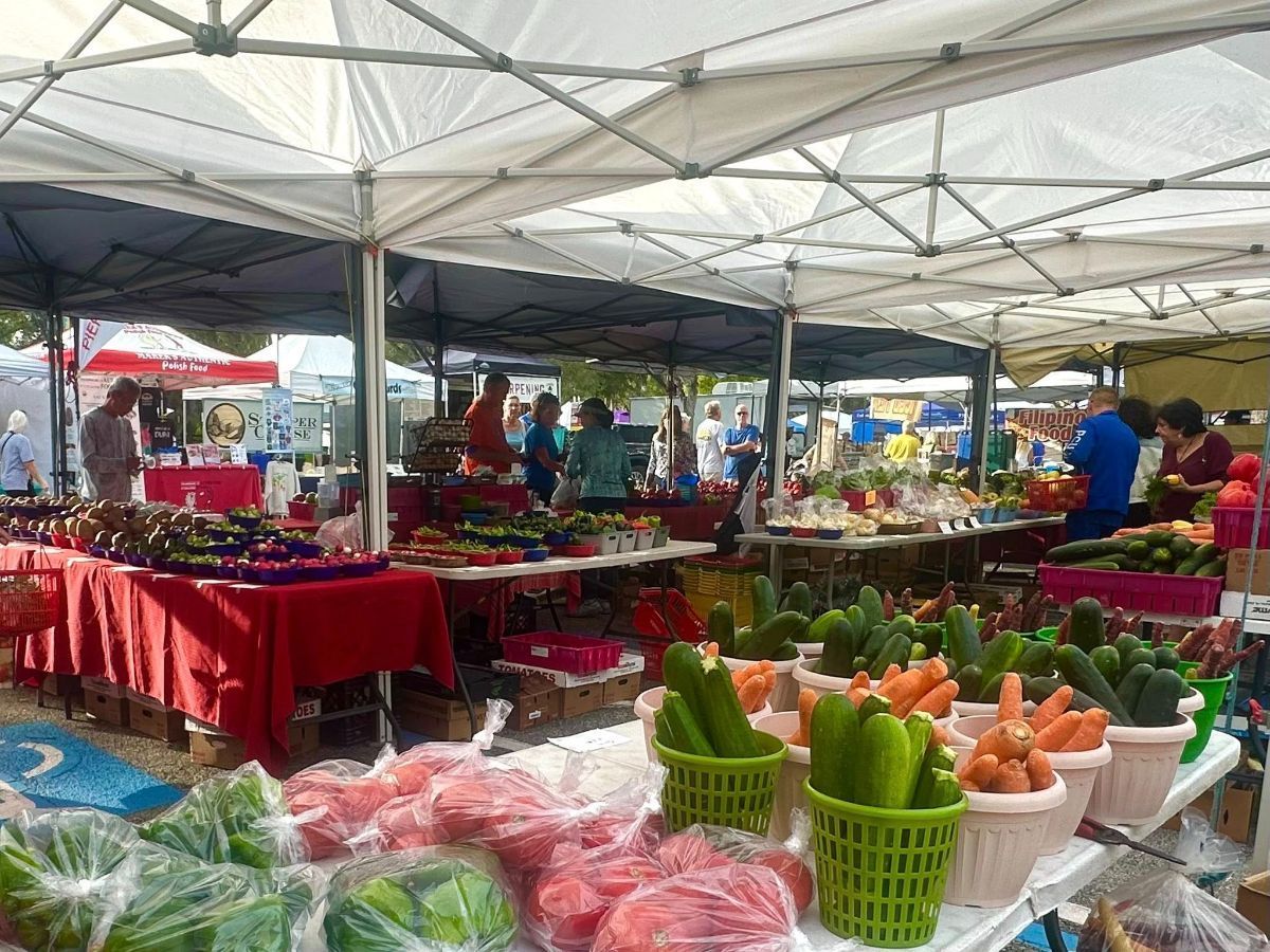 Farmers market with various produce on display under tent canopies.