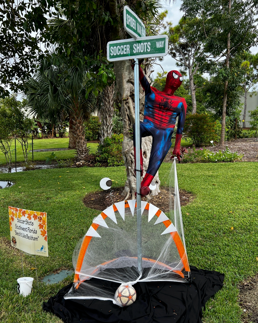A spiderman statue is standing next to a soccer goal in a yard.