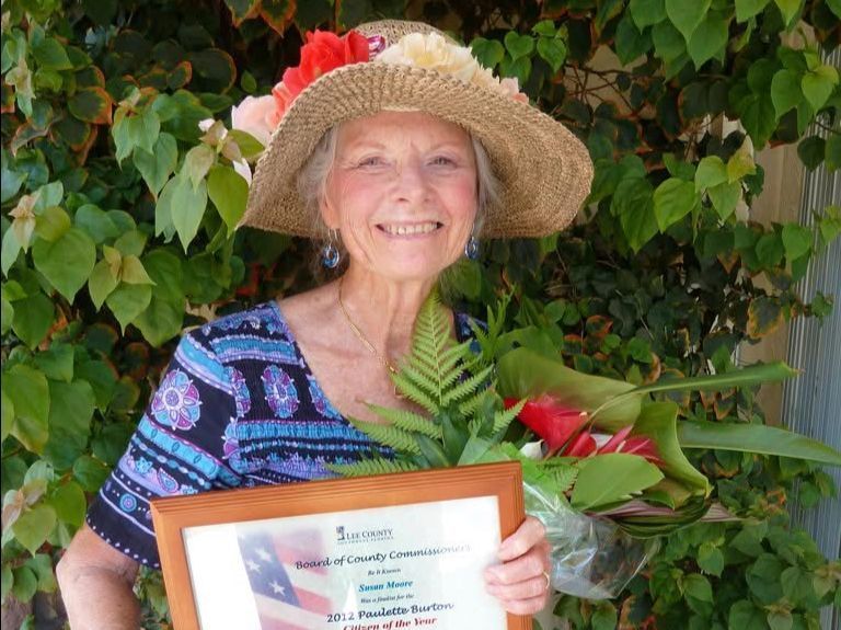 A woman in a straw hat is holding a framed certificate