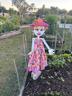 A scarecrow in a pink dress and hat is standing in a garden.