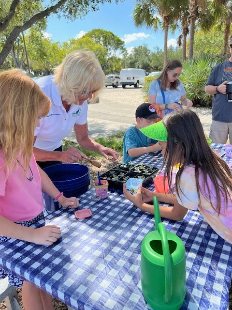 A group of children are sitting at a table with a watering can.