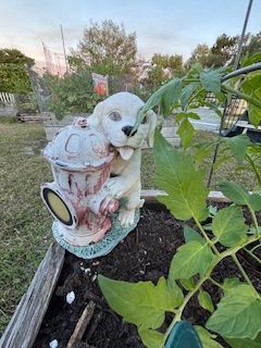 A statue of a dog holding a fire hydrant in a garden.