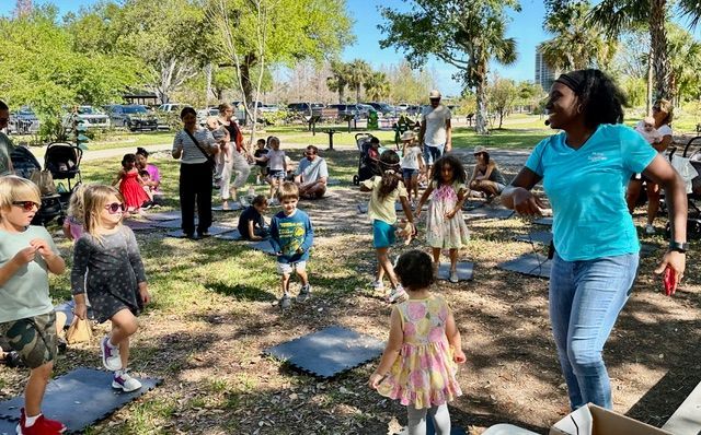 A woman is dancing with a group of children in a park.