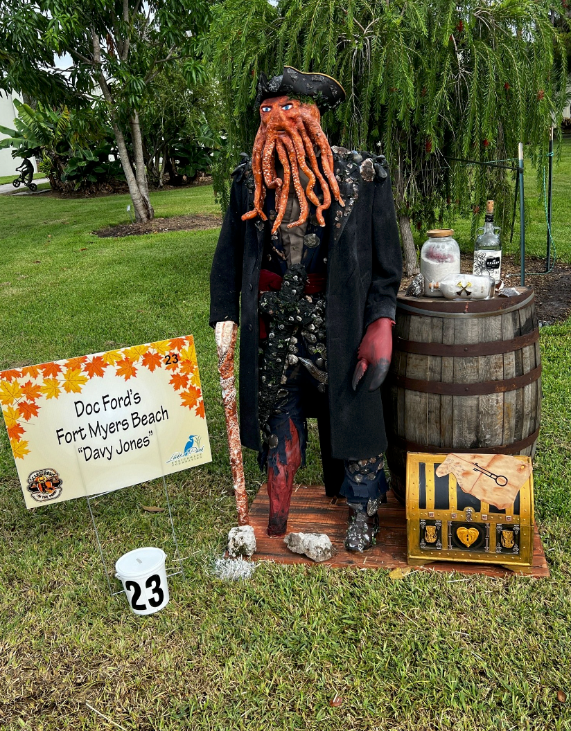 A scarecrow dressed as a pirate is standing in the grass next to a sign.