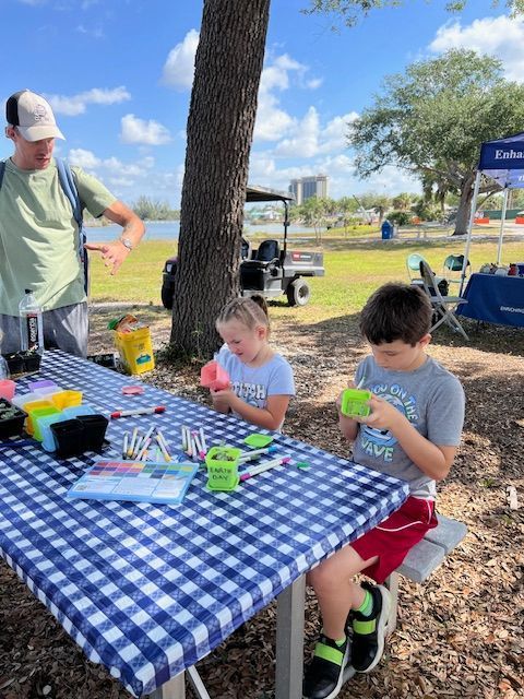 Two children are sitting at a picnic table with a man standing behind them.