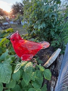 A red glass bird is sitting on top of a plant in a garden.
