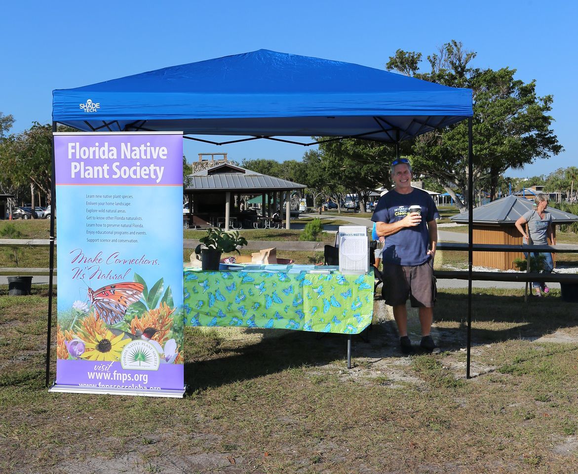A man is standing under a blue tent with a sign that says florida native plant society