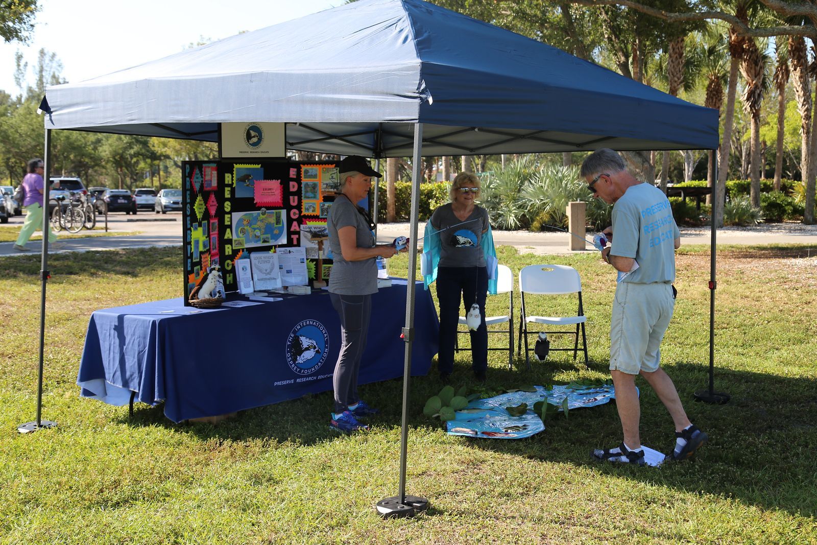 A man and a woman are standing under a blue tent in a park.