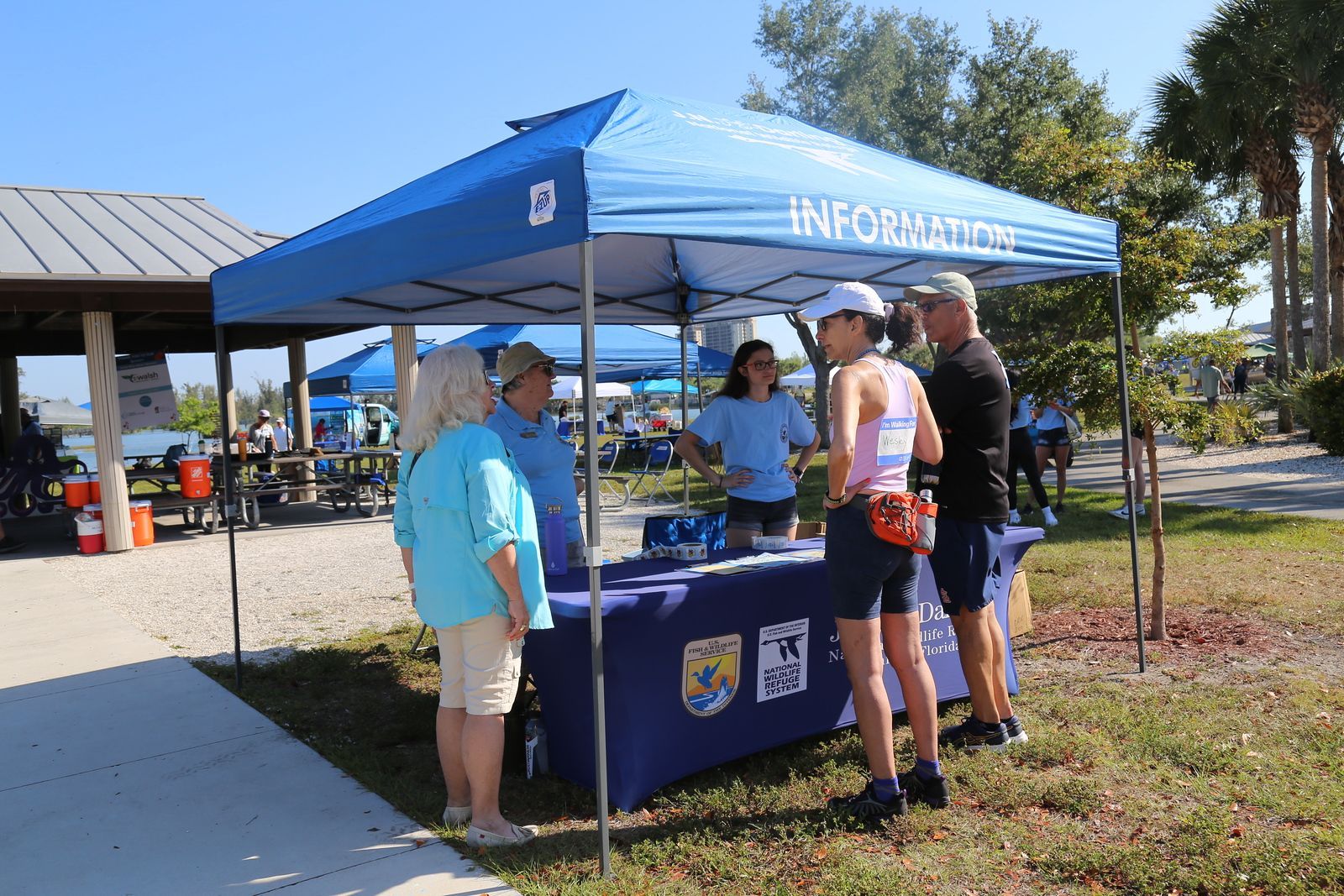 A group of people are standing around a table under a blue tent.