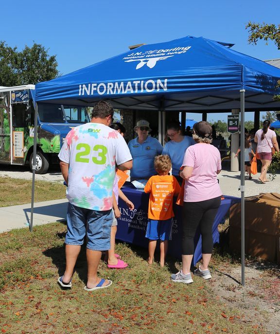 A group of people standing under a blue tent that says information