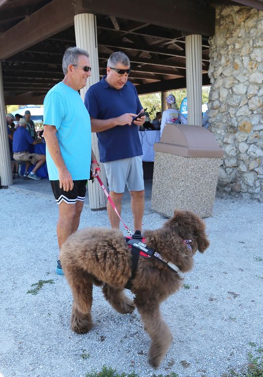 Two men are standing next to a large brown dog on a leash.