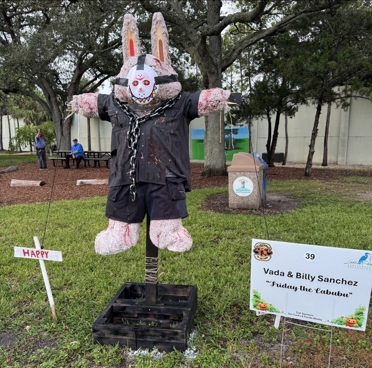 Scarecrow dressed as Jason Voorhees with bunny ears, standing in a park.