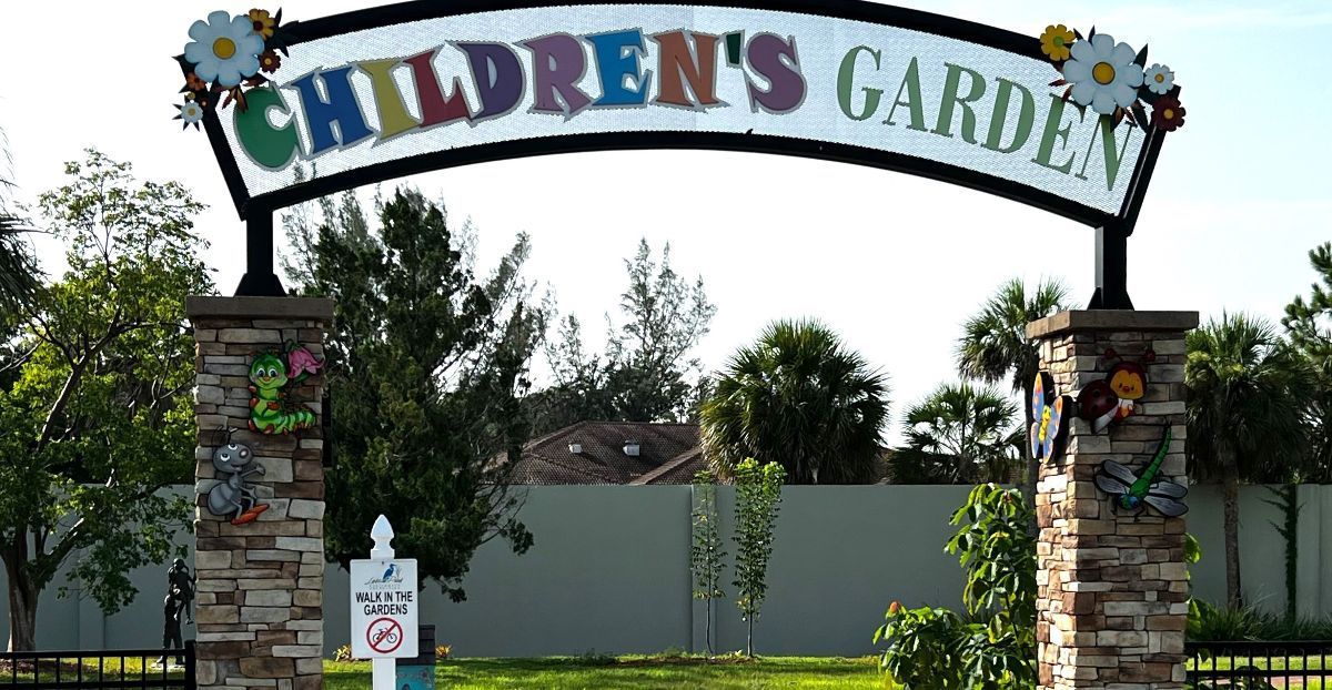 Entrance to Children's Garden with a colorful sign and stone pillars. Flowers decorate the entrance.