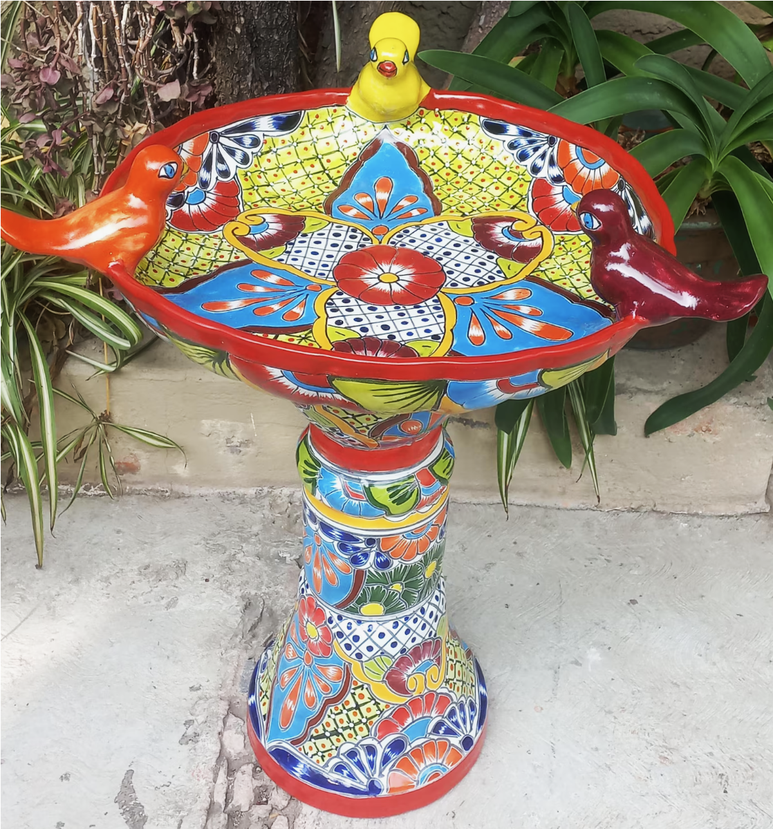 Colorful, ornate ceramic birdbath with red, blue, and yellow patterns, topped with a yellow duck.