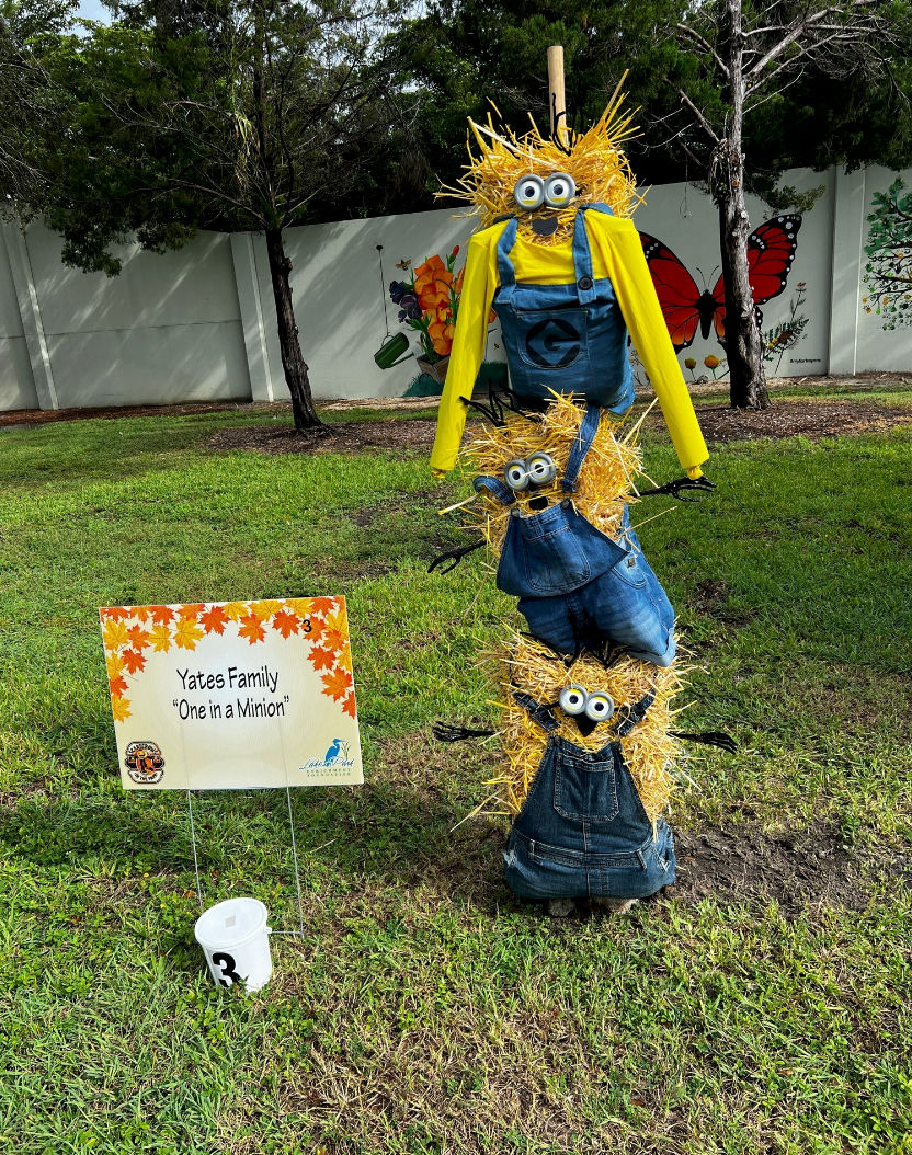 A scarecrow made out of hay is standing in the grass next to a sign.