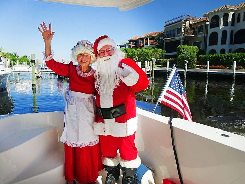 A man and a woman dressed as santa claus are standing on a boat.