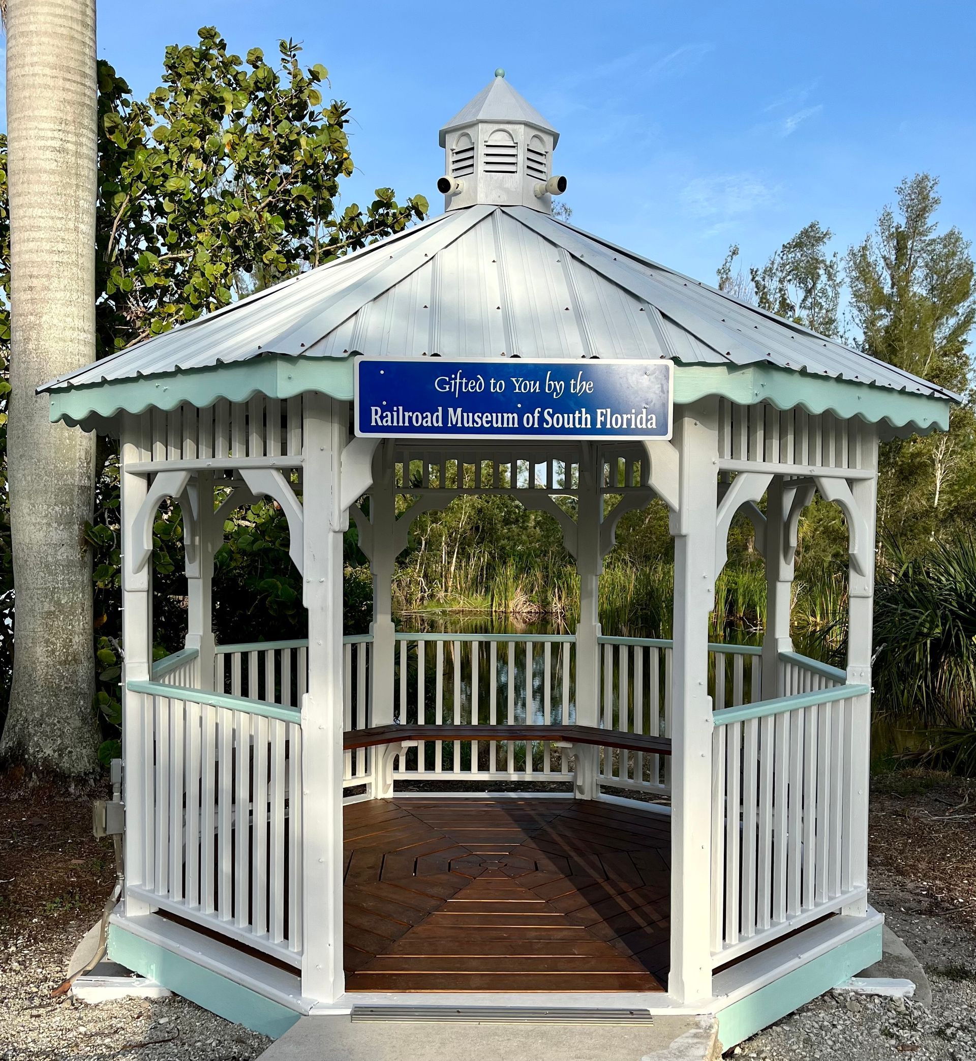 A white gazebo with a blue sign that says welcome