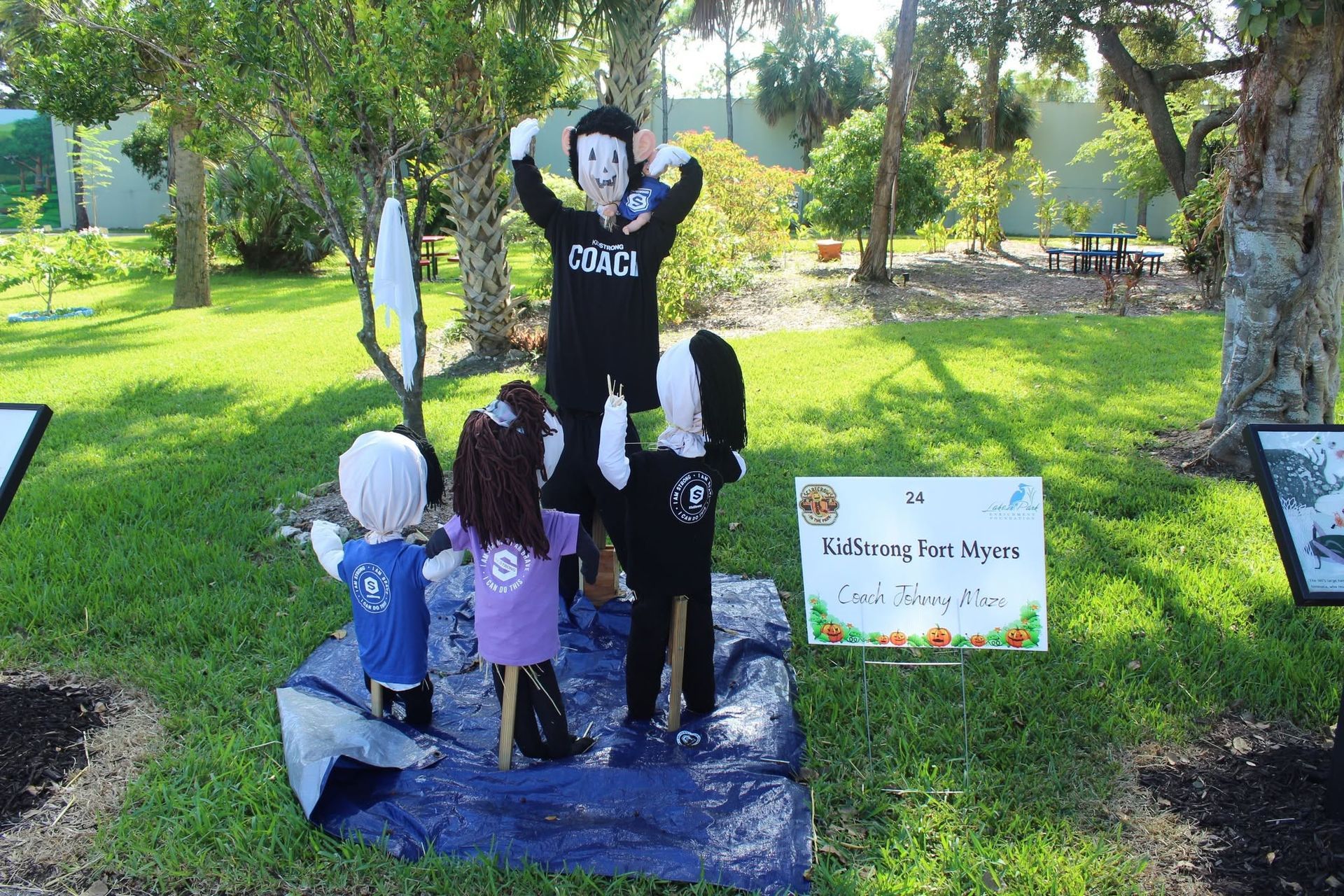 Two people in black-and-white costumes posing on a park display platform beside a sign and small figures