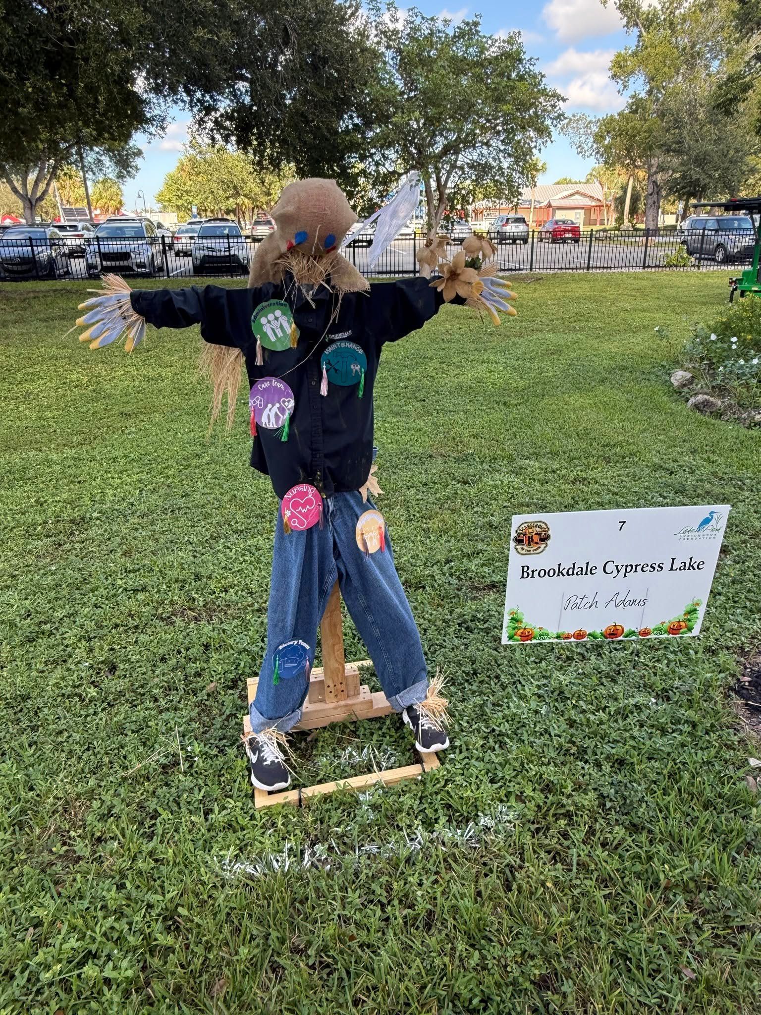 Scarecrow on a wooden base in a grassy park, decorated with colorful flowers and butterflies.