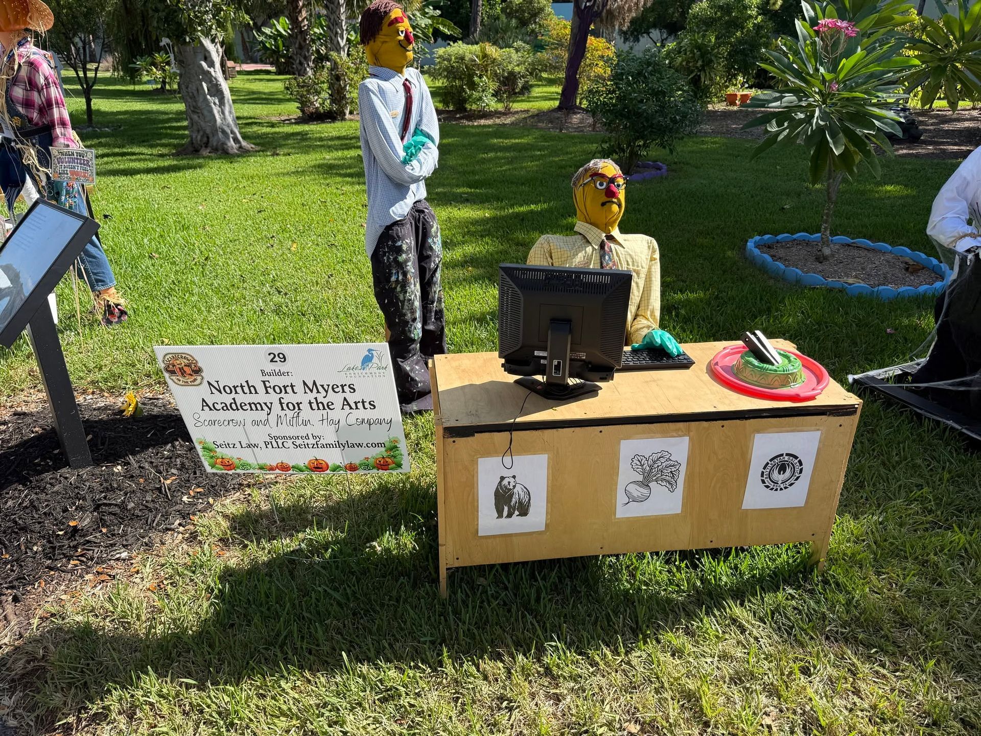 Outdoor display table with monitor and handwritten sign in a grassy park area