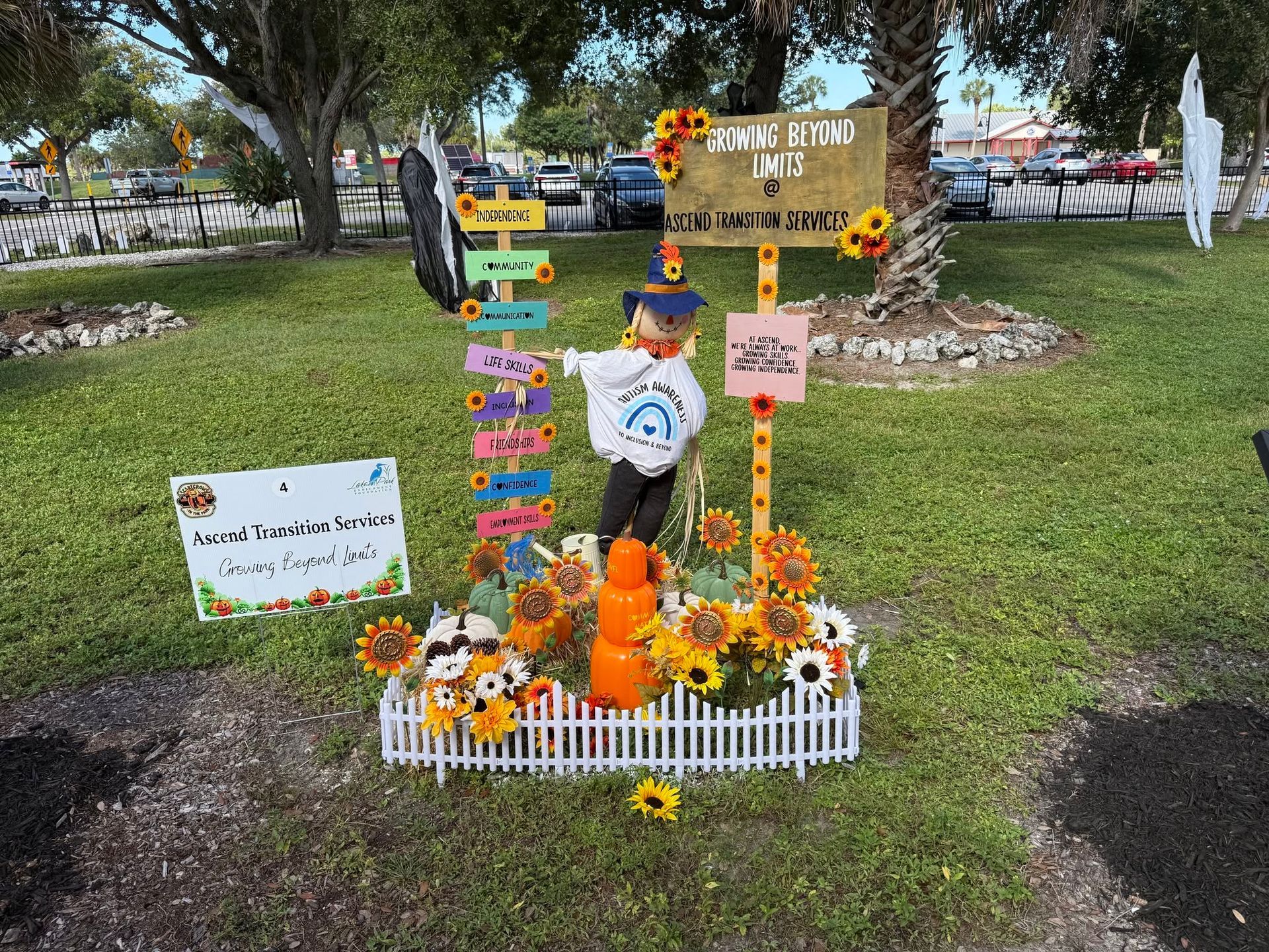 Child at a colorful fall memorial display with pumpkins, sunflowers, and a small white fence in a grassy park.