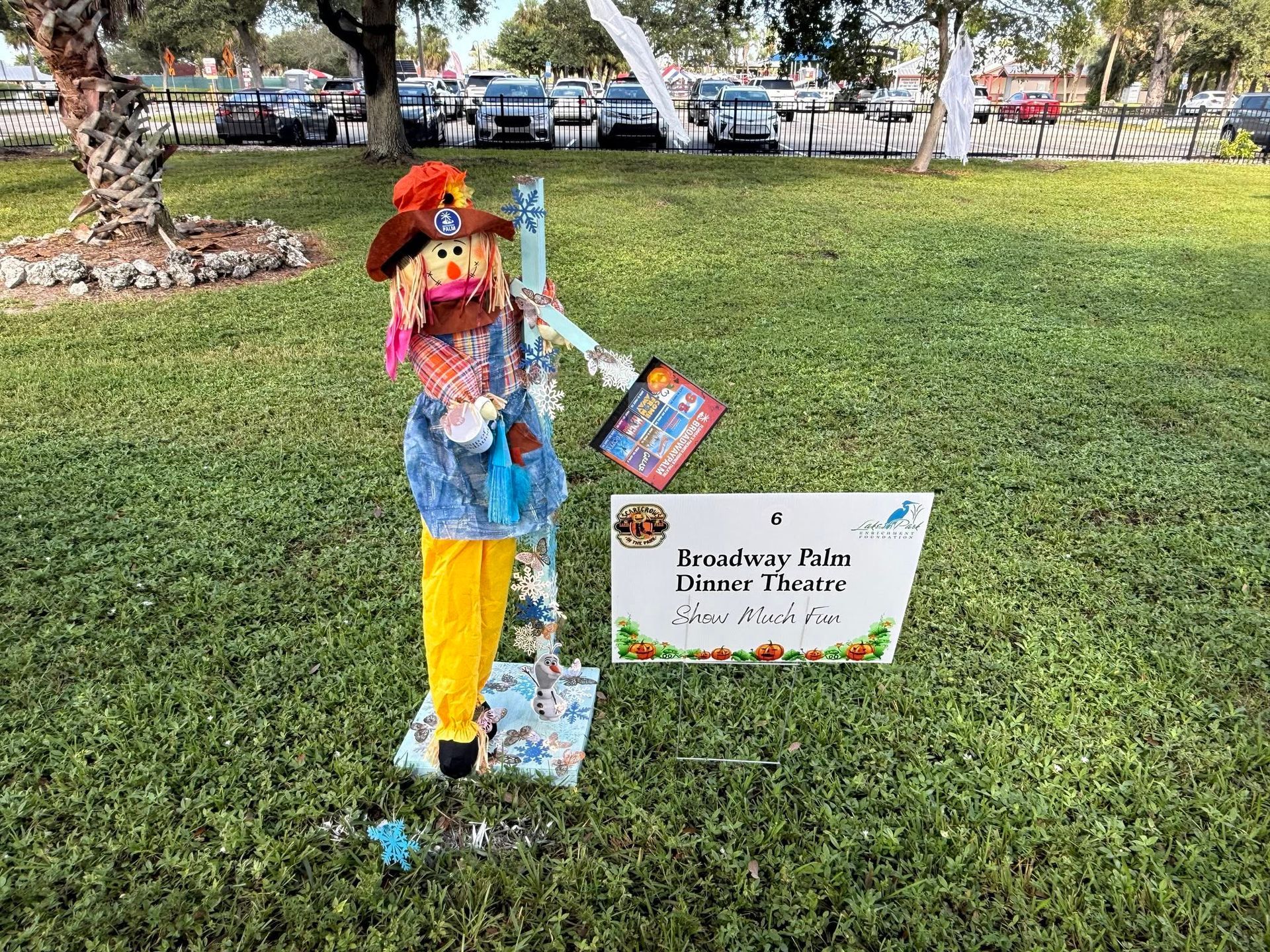 Decorated child scarecrow display on a grassy lawn beside a small sign.