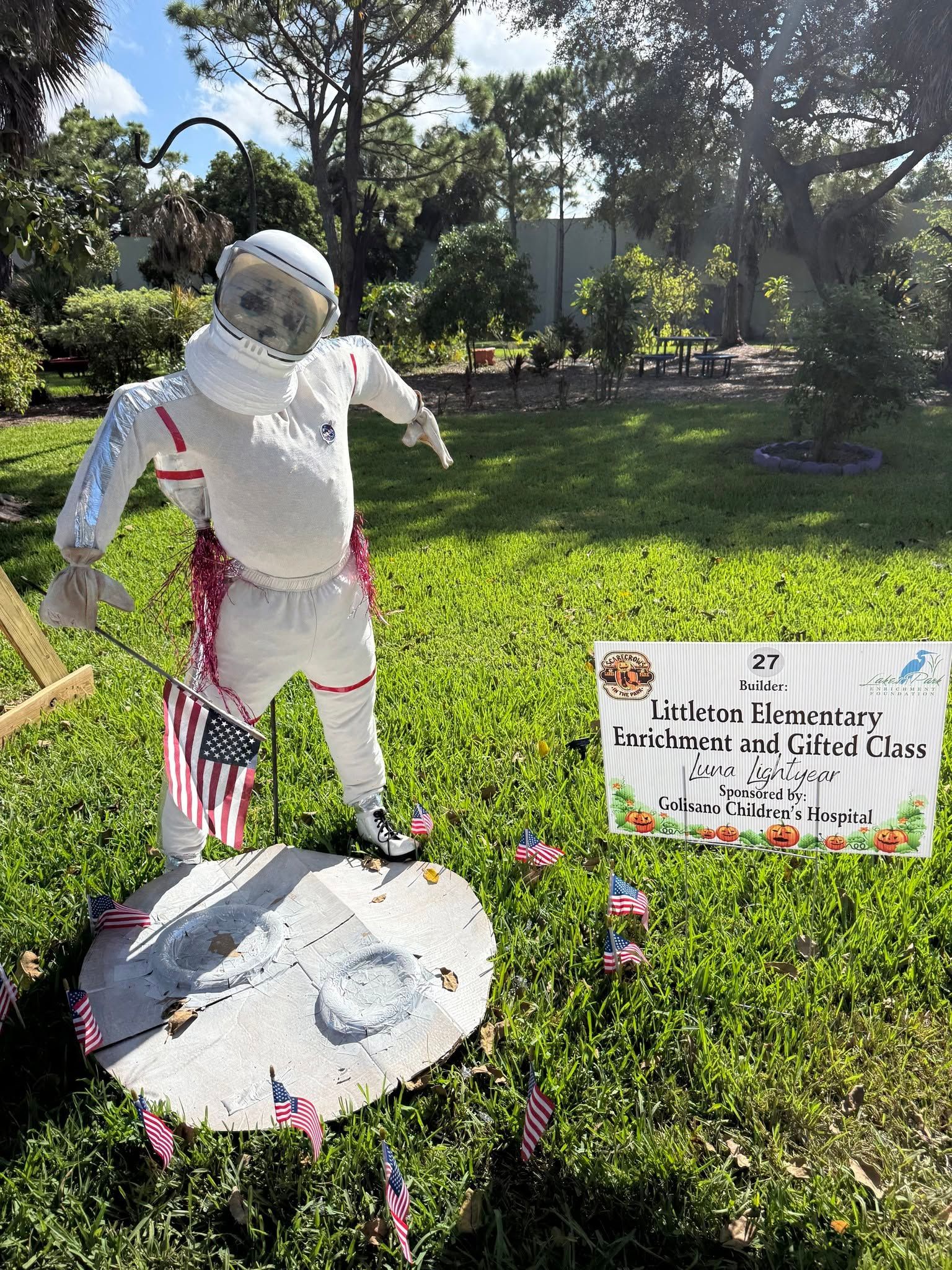 White knight-like Halloween figure on a lawn beside a small sign and decorated ground display.