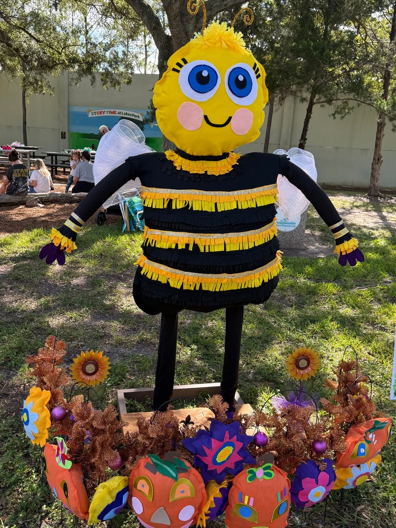 Bee costume figure in a garden display with colorful flowers and pumpkins