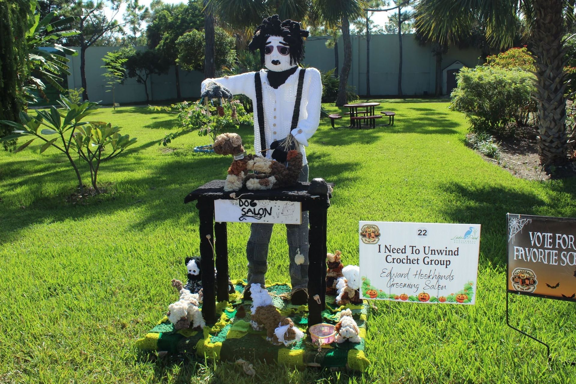 Charlie Chaplin-style statue in a sunny garden, surrounded by flowers and memorial signs.