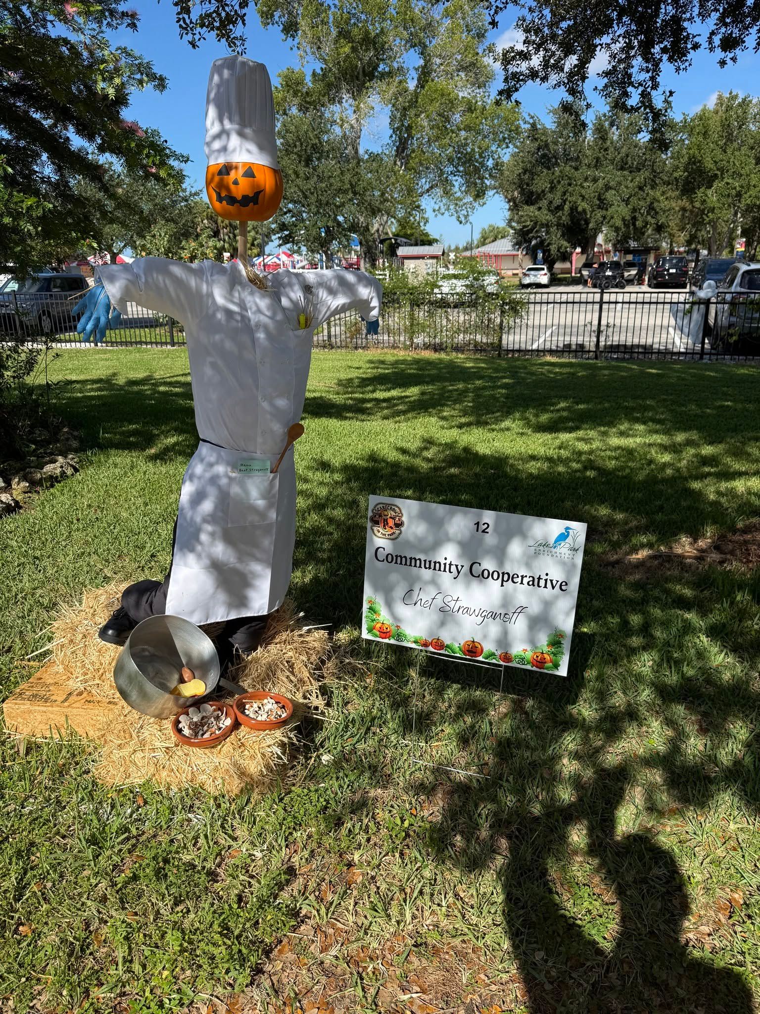 Homemade scarecrow in a grassy yard with a sign beside it on a sunny day