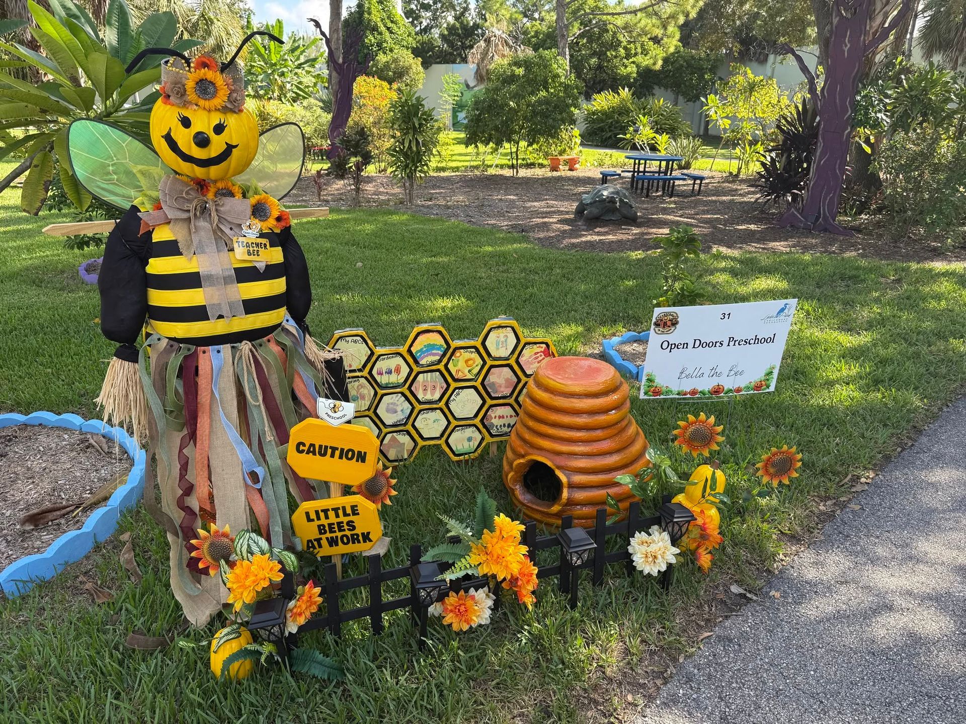 Halloween bee scarecrow with honeycomb, flowers, caution sign, and pumpkins in a garden display