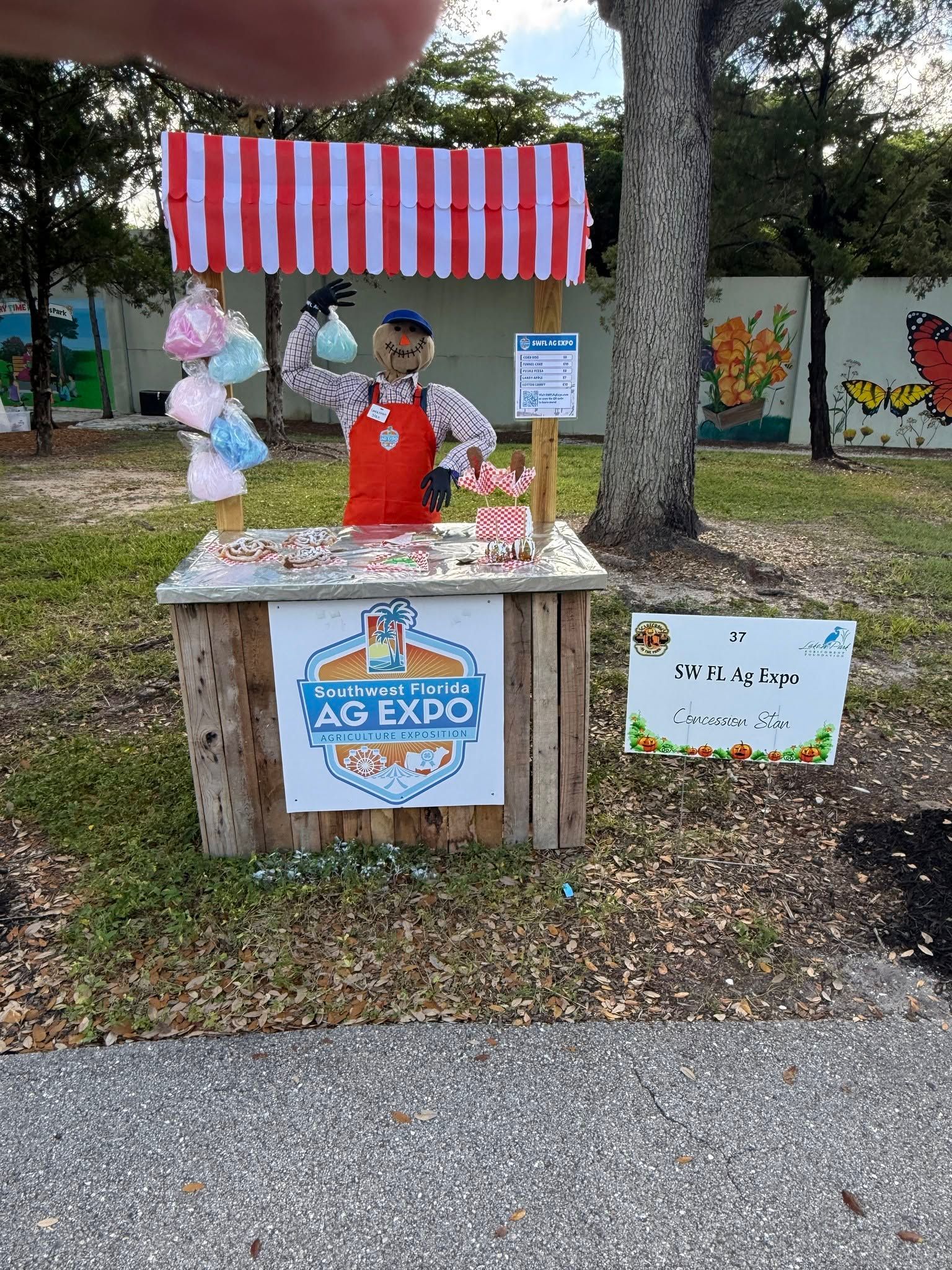 Outdoor candy stand with red-and-white striped canopy, decorated jars, and a person serving treats at a festival booth
