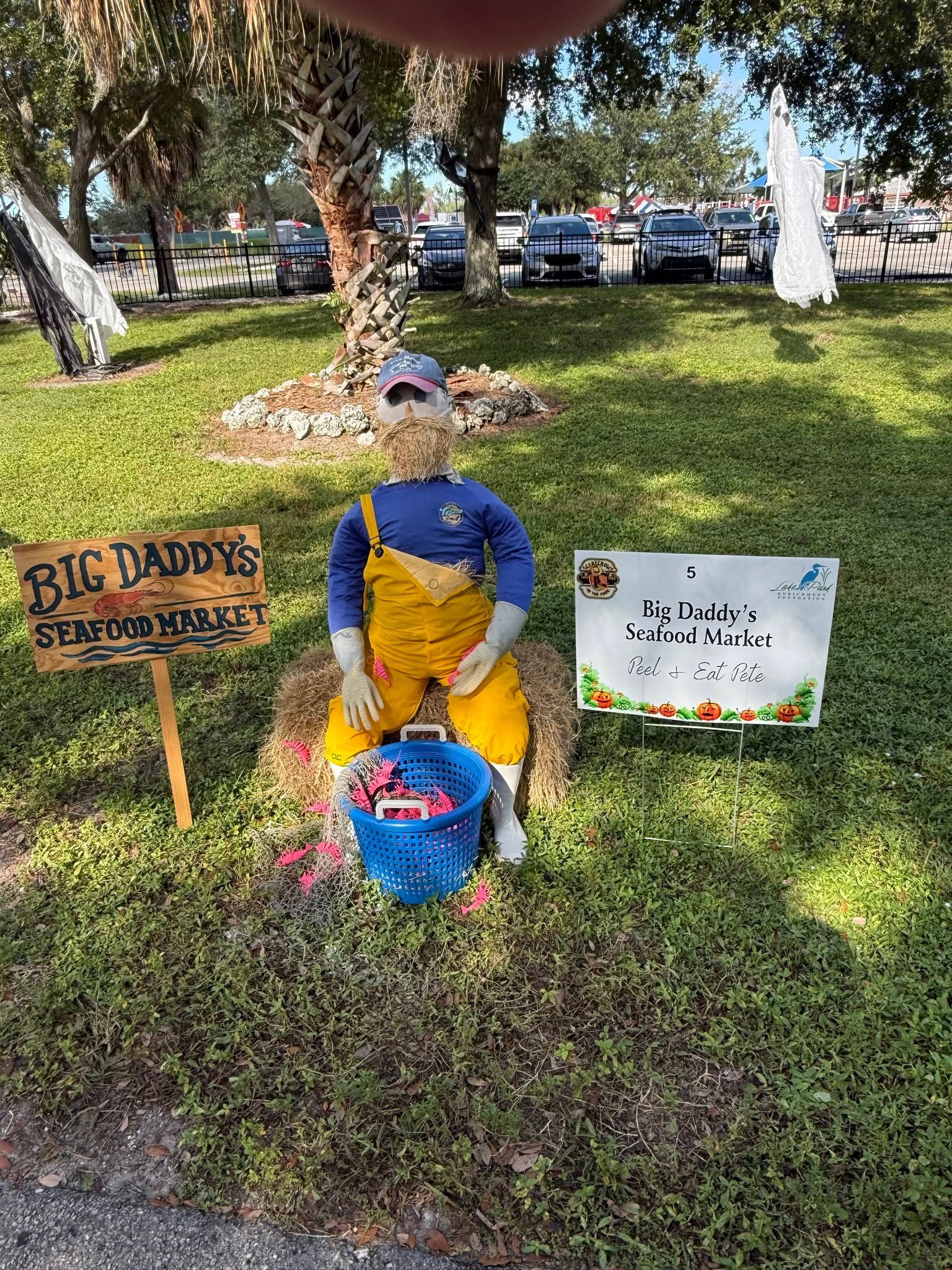 Decorated dog memorial display with a blue-and-yellow figure, flowers, and signs in a grassy park area