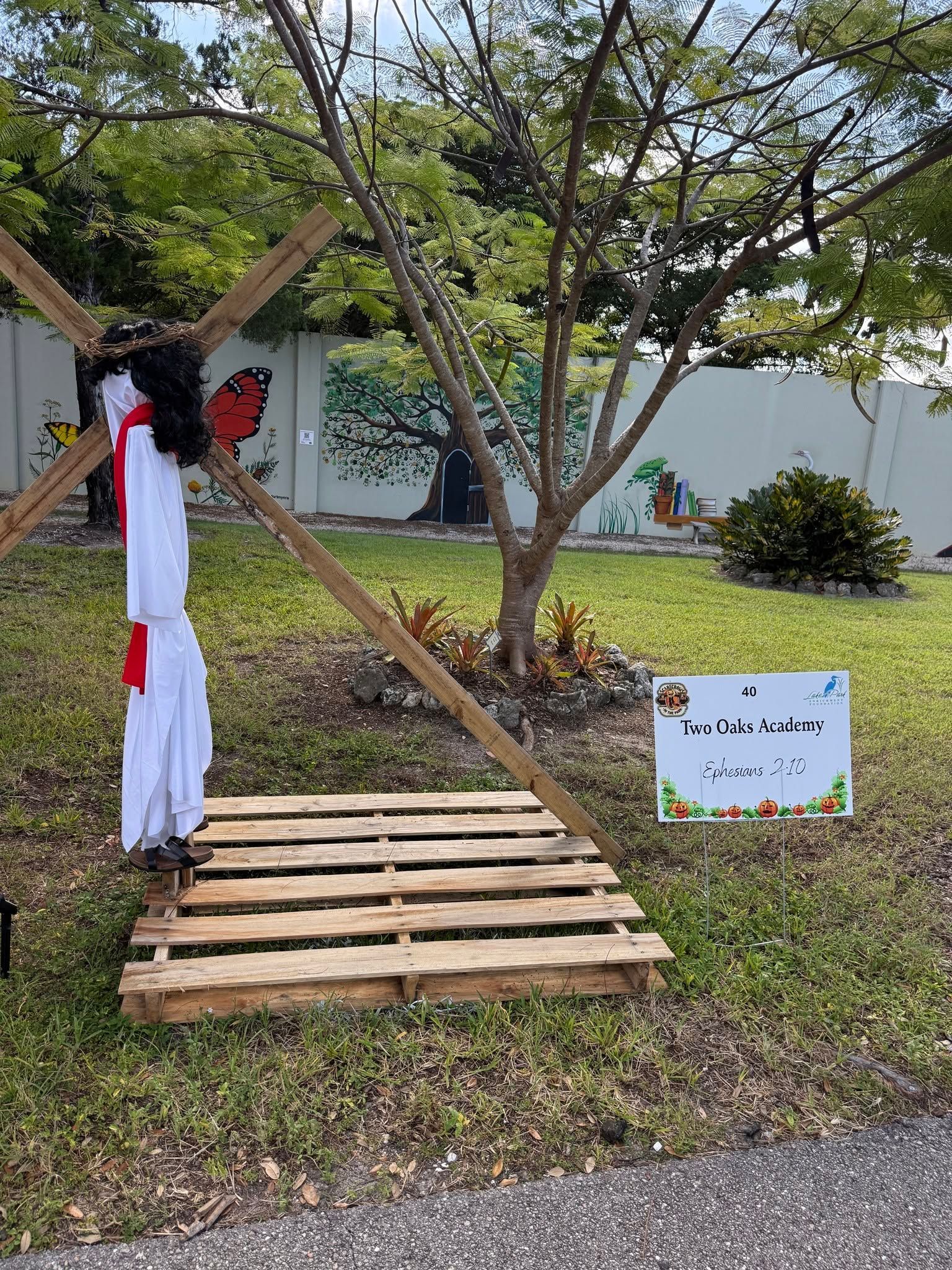Decorated white scarecrow on a wooden pallet path in a grassy yard with a sign nearby
