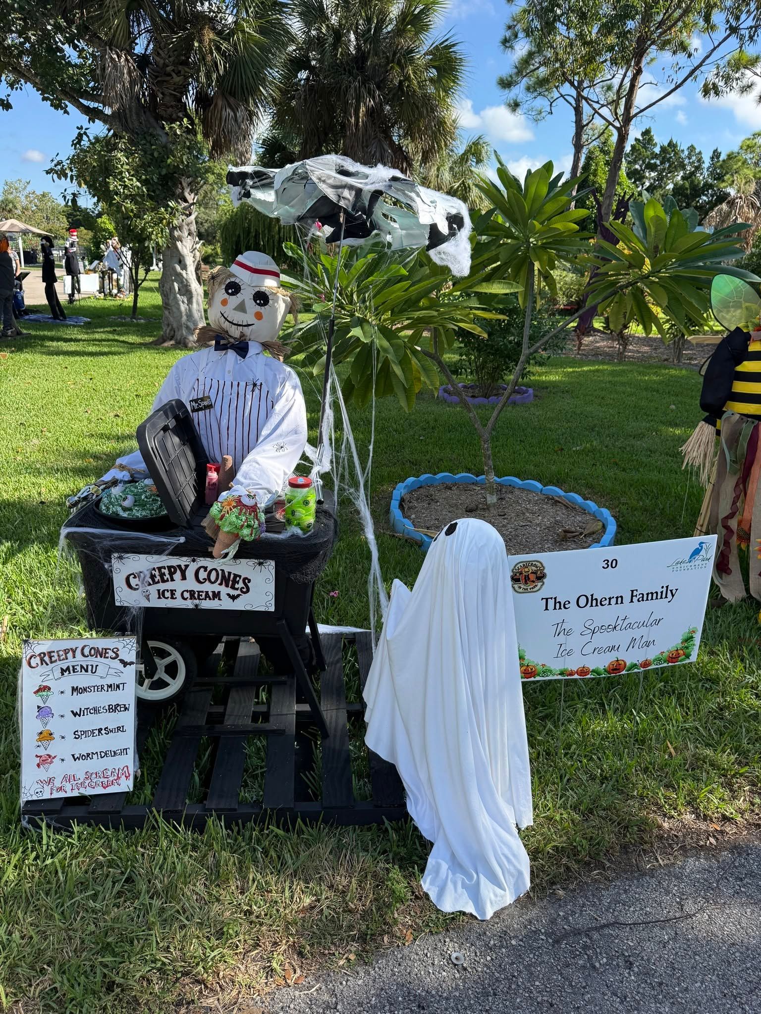 Person in white costume sitting beside a ghost figure outdoors in a grassy park display