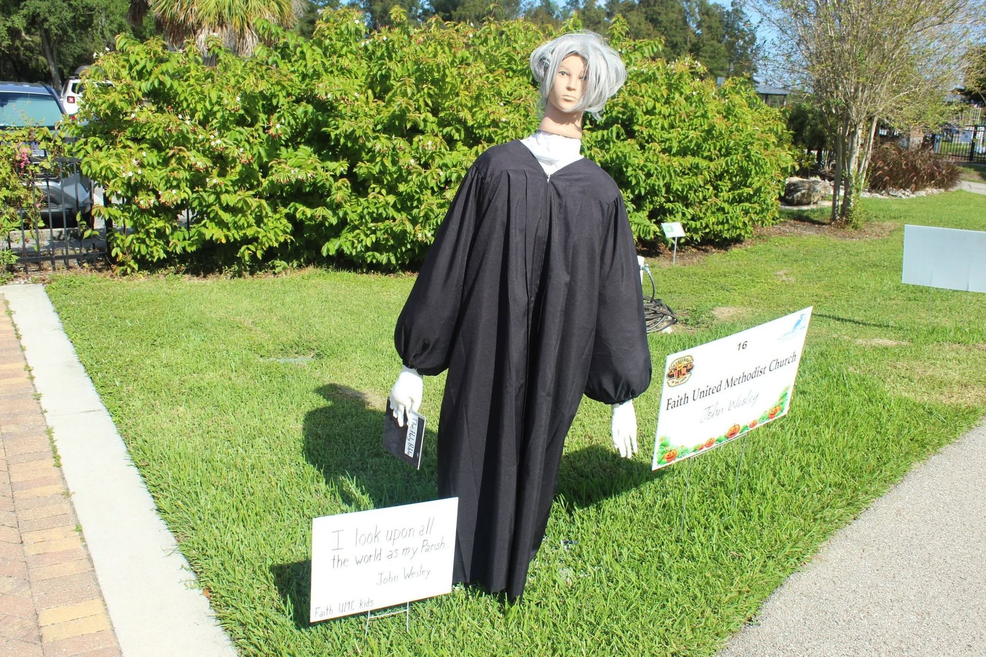 Mannequin in a black graduation gown on a grassy lawn with signs beside it