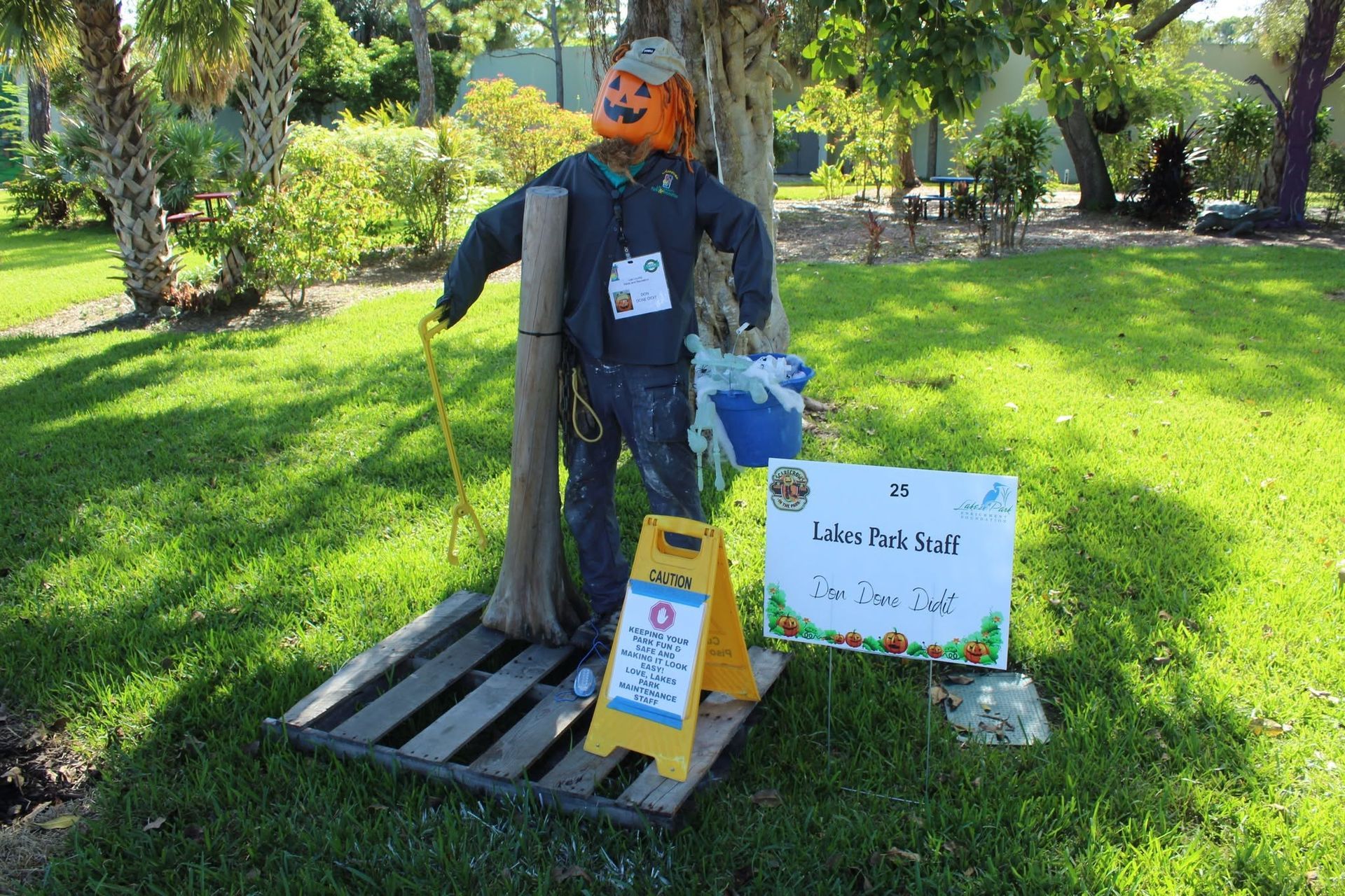 Person sitting on a pallet in a sunny park beside a sign and donation items