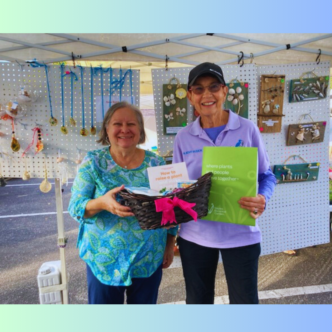 Two women are standing under a tent holding a basket and a book