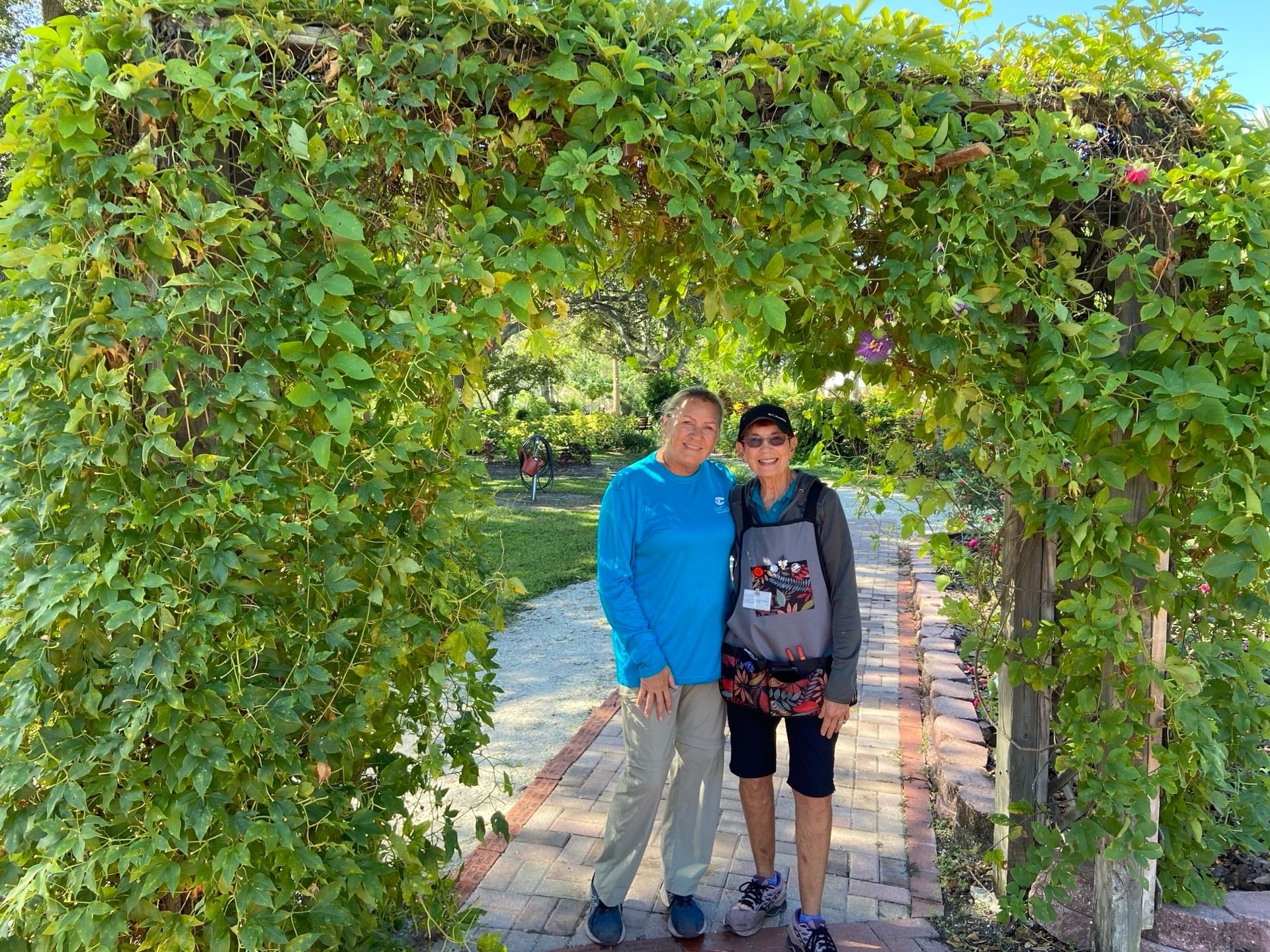 Two people are standing under a green archway in a park.