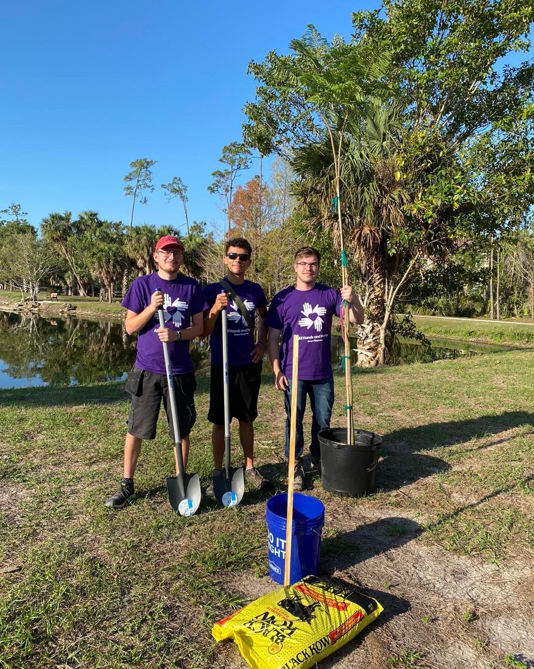 Three men are standing next to each other in a field holding shovels.