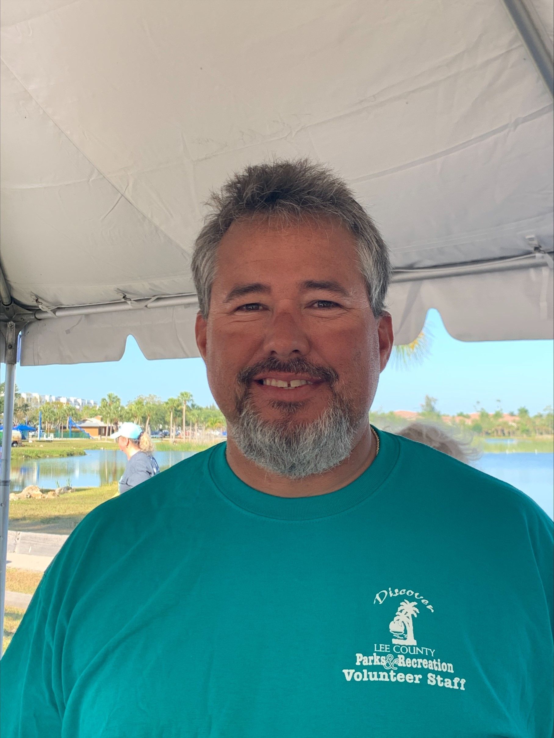 A man with a beard is wearing a green shirt and smiling.