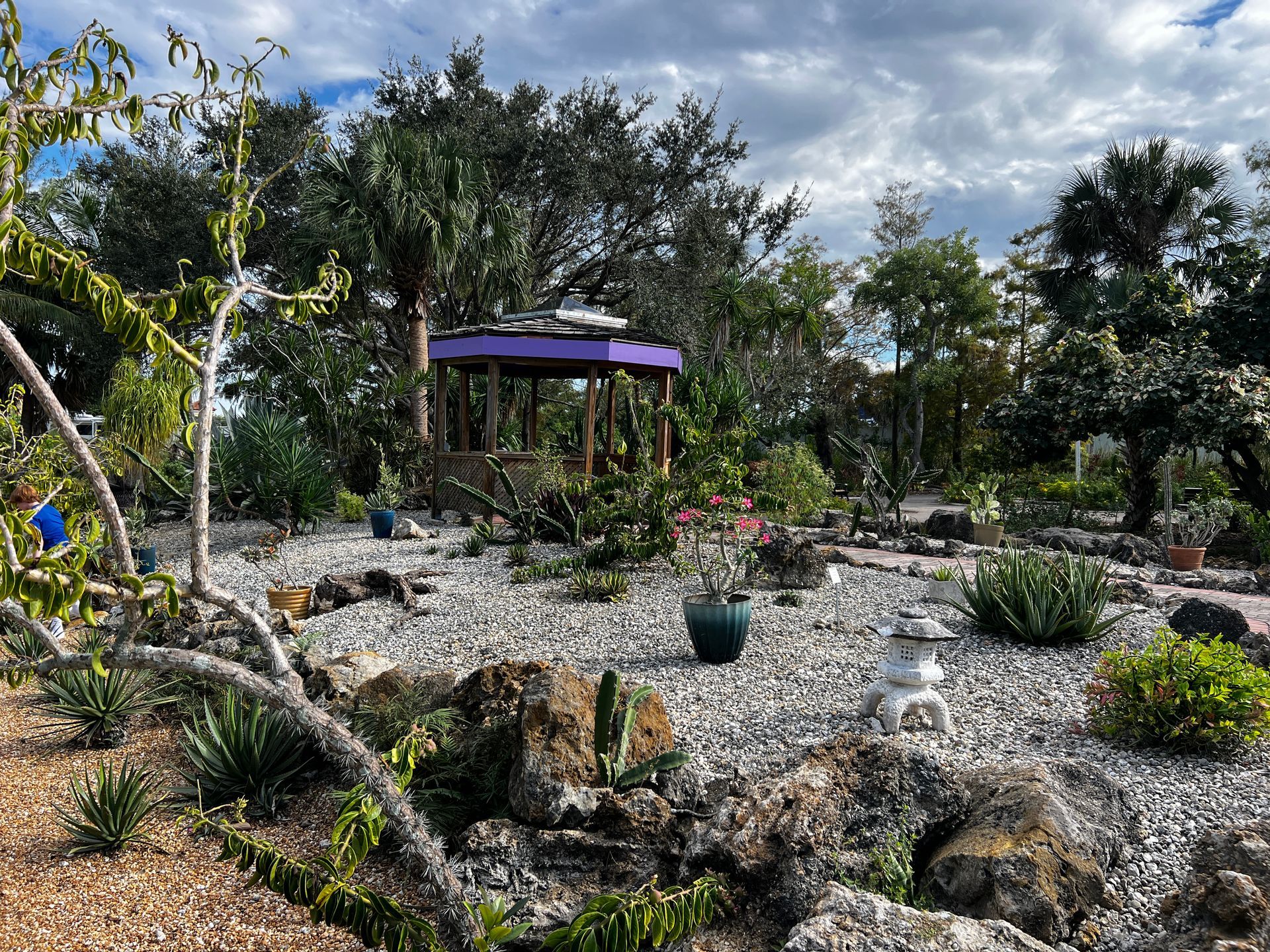 There is a gazebo in the middle of the garden surrounded by rocks and trees.